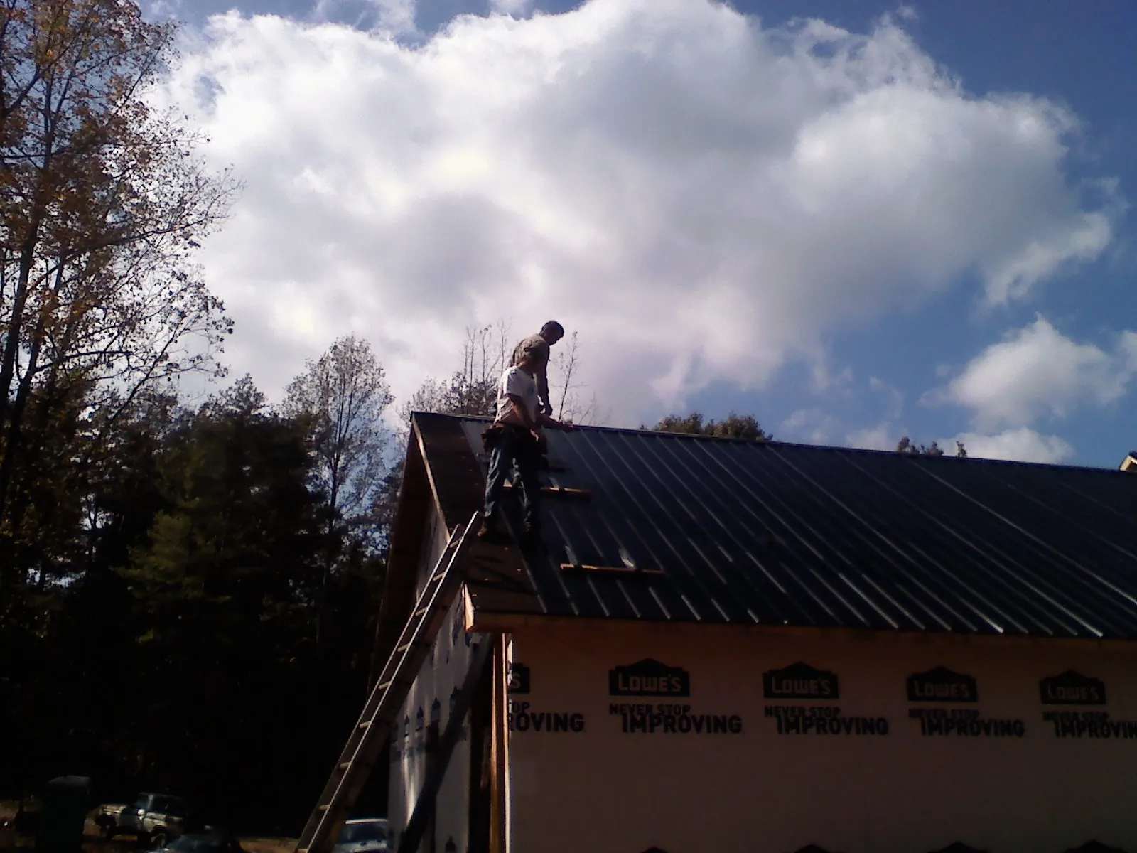 Roofer fastening dark metal panels high against a cloudy sky, from a Roof Inspection job in Harrison